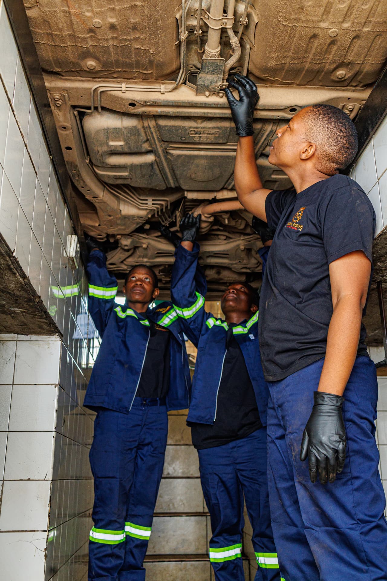 Three technicians inspecting a vehicle underbody on the ramp